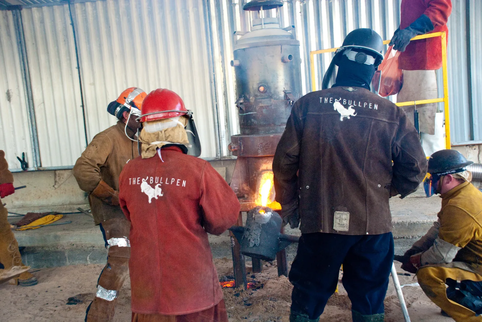 A team in Bullpen jackets catching molten iron from the furnace in a ladle